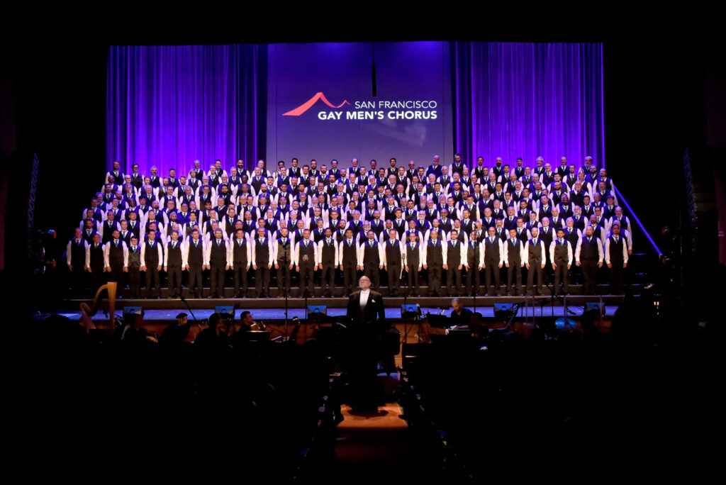 The San Francisco Gay Men’s Chorus performs onstage under purple lighting in Unbreakable.